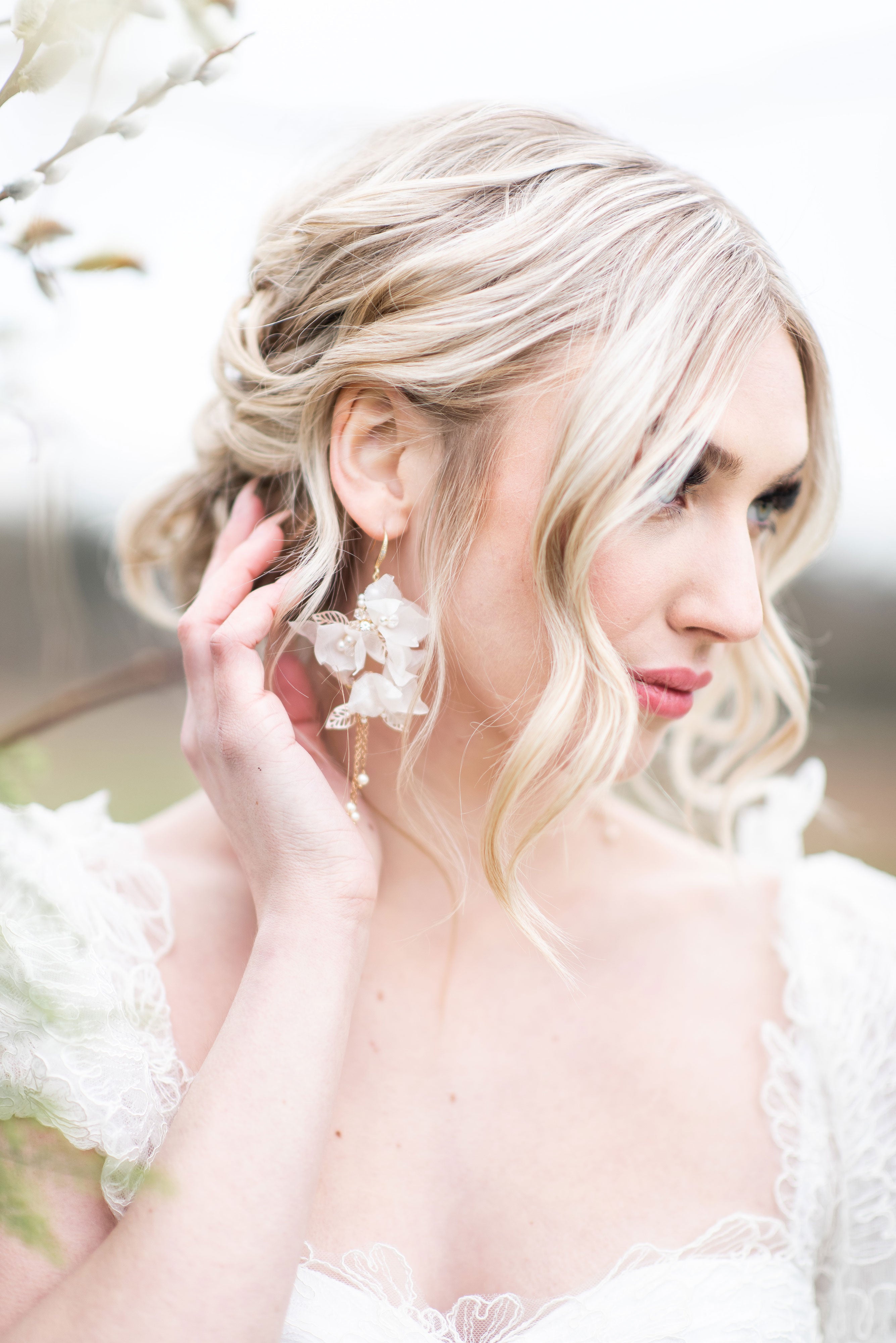 Elegant bride with a romantic updo hairstyle, showcasing a unique floral earring. The delicate earring design complements her lace bridal gown, embodying a soft and sophisticated wedding look.