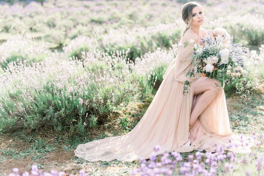 Boho bridal silhouette in a lavender field, featuring an elegant bride in a flowing peach gown with a large floral bouquet, perfect for a bohemian wedding style