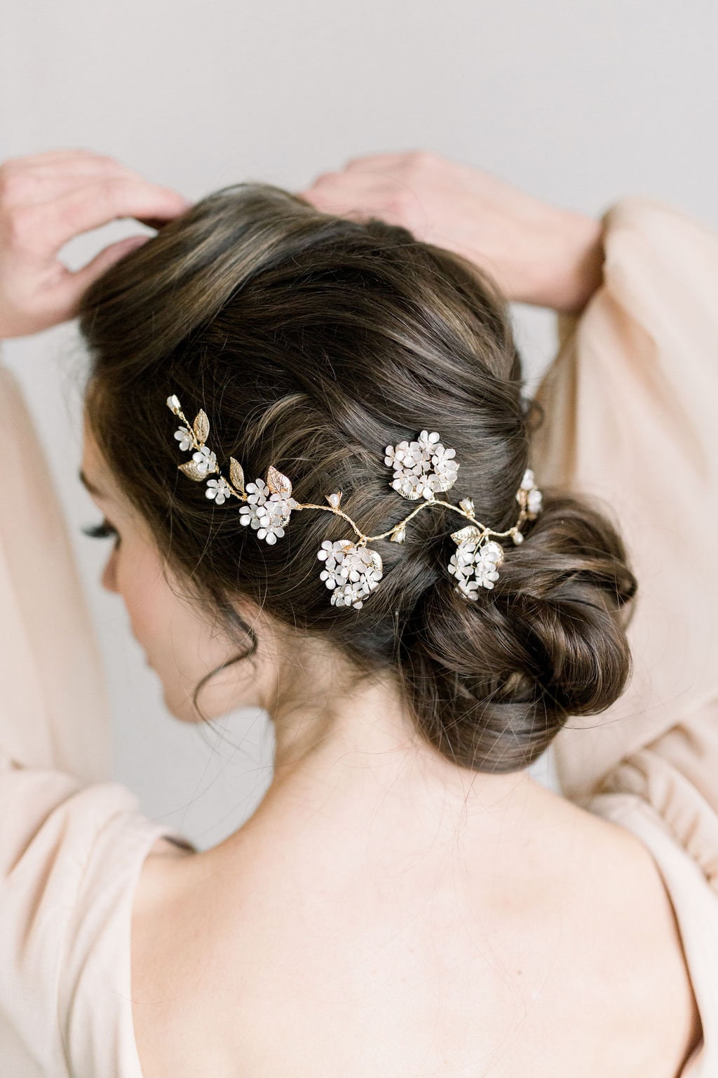 Elegant bridal updo accented with a delicate floral hairpiece featuring crystal centers and gold accents. This sophisticated hairstyle showcases intricate twists and turns, perfectly complementing a luxurious wedding look.